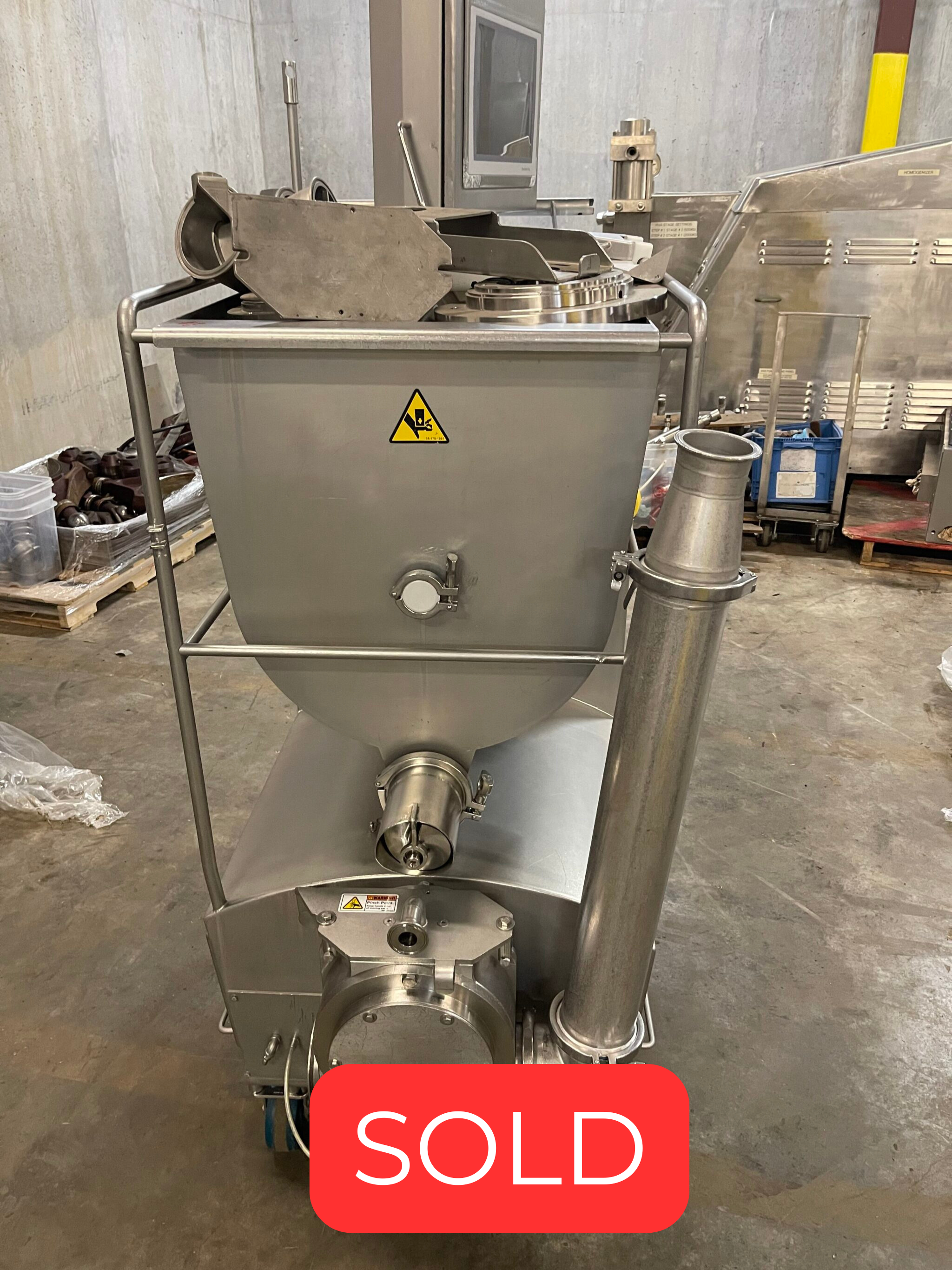 Industrial stainless steel mixer with a conical hopper and discharge chute on a metal frame in a workshop.